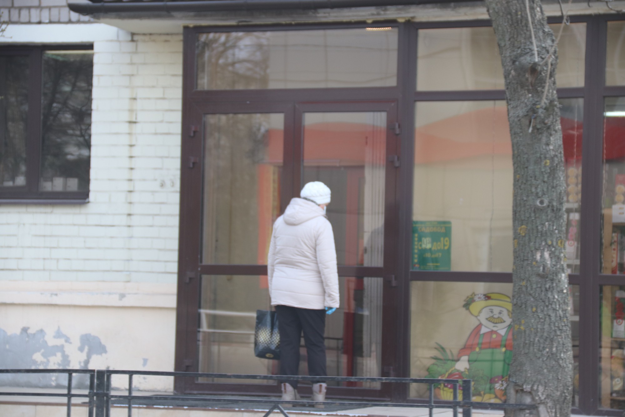 Женщина смотрит на витрины закрытого магазина семян